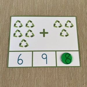May include: A white card with green recycling symbols and the equation 6 + 3 = 9. The answer 9 is written in blue on the card. A green circle with the number 8 written in white is on the card.