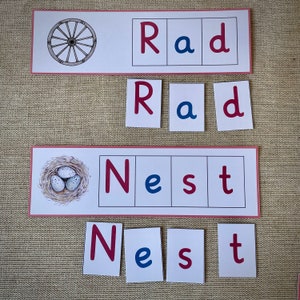 May include: A set of red and blue letter tiles spelling out the words "Rad" and "Nest". The tiles are arranged in a grid pattern. There is a picture of a wagon wheel above the "Rad" tiles and a picture of a bird's nest with eggs above the "Nest" tiles.