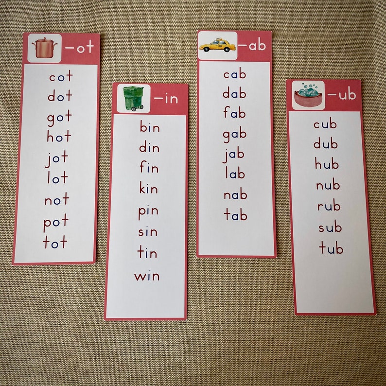 May include: Four red and white flashcards with different images and words. The first card has a red pot with a lid and the word "cot, dot, got, hot, jot, lot, not, pot, tot" written below. The second card has a green recycling bin and the word "bin, din, fin, kin, pin, sin, tin, win" written below. The third card has a yellow taxi cab and the word "cab, dab, fab, gab, jab, lab, nab, tab" written below. The fourth card has a red tub with bubbles and the word "cub, dub, hub, nub, rub, sub, tub" written below.
