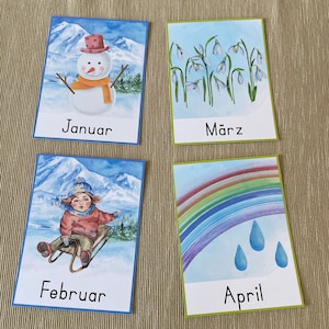 May include: Four illustrated cards depicting the months of January, February, March, and April. January shows a snowman, February shows a child sledding, March shows a field of snowdrops, and April shows a rainbow with raindrops.