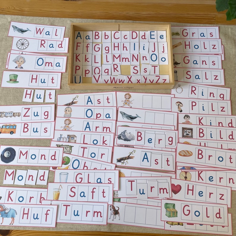 May include: A set of colourful flashcards with German words and pictures. The words include "Wal", "Rad", "Oma", "Hut", "Zug", "Bus", "Mond", "Korb", "Huf", "Ast", "Opa", "Arm", "Lok", "Tor", "Glas", "Saft", "Turm", "Gras", "Holz", "Gans", "Salz", "Ring", "Pilz", "Kind", "Bild", "Brot", "Kern", "Herz", "Gold", and "Berg".
