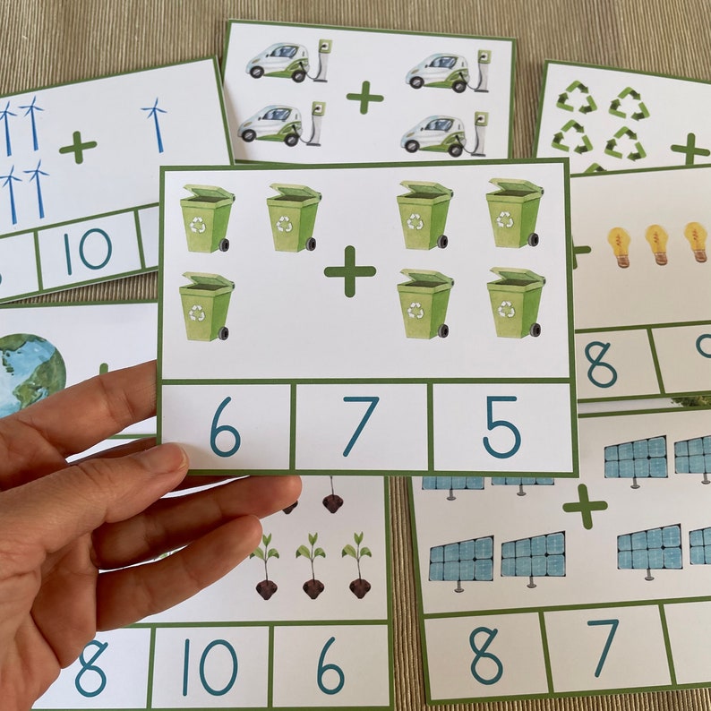 May include: A set of green and white flashcards with math problems featuring images of recycling bins, wind turbines, solar panels, light bulbs, and plants. The numbers 6, 7, 5, 8, 10 are written on the cards.