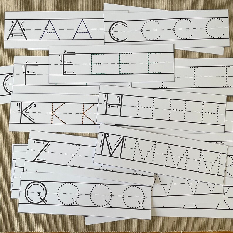 Op de afbeelding: Een set alfabet-traceerkaarten met de hoofdletters A, C, E, H, K, M, Q en Z. Elke kaart heeft een stippellijn om de letter te traceren en genummerde pijlen om de gebruiker te begeleiden.