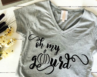 Op de afbeelding: Grijs V-hals T-shirt met de tekst "Oh my gourd" in zwarte schrijfletters met een kleine pompoenafbeelding.