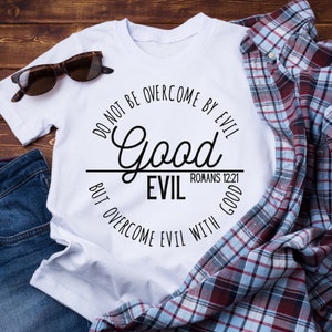 Könnte beinhalten: Weißes T-Shirt mit einem schwarzen Kreis-Motiv, auf dem steht: "Lasst euch nicht vom Bösen überwinden, sondern überwindet das Böse mit Gutem." Das Motiv enthält auch den Text "Good" in größerer Schrift und "Evil" in kleinerer Schrift. Der Text "Römer 12:21" ist ebenfalls im Motiv enthalten.