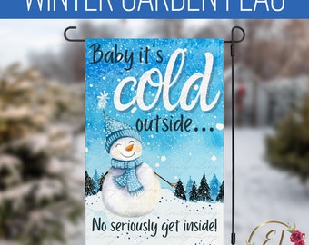 Op de afbeelding: Een wintertuin vlag met een sneeuwpop en de tekst "Baby it's cold outside... No seriously get inside!" op een blauwe achtergrond met witte sneeuwvlokken.