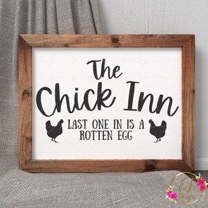 以下が含まれることがあります： 白い背景に黒い文字で「The Chick Inn Last One In Is A Rotten Egg」と書かれた、木製の素朴なフレームの看板。文字の両側に黒い鶏のシルエットが2つある。