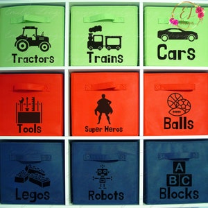 Puede incluir: Nueve cestas de almacenamiento de tela con etiquetas e iconos negros. Las etiquetas dicen: Tractores, Trenes, Coches, Herramientas, Superh&eacute;roes, Pelotas, Legos, Robots y Bloques. Los iconos representan un tractor, un tren, un coche, herramientas, un superh&eacute;roe, una pelota de baloncesto y una pelota de f&uacute;tbol, bloques de Lego, un robot y bloques de letras.