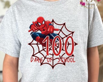 May include: A light gray t-shirt featuring a graphic of Spider-Man in a web design with the number 100 in red. The text "DAYS OF SCHOOL" is below the number. The shirt has a crew neck.