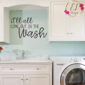 May include: A white laundry room with a white cabinet and a white washing machine. The wall is light blue and has a black vinyl decal that says "it'll all come out in the wash".
