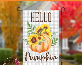 May include: A garden flag with a watercolor design featuring a pumpkin and sunflowers. The flag has the words "HELLO PUMPKIN" and "INSTANT DOWNLOAD" printed on it. The background is a gray and white plaid pattern.
