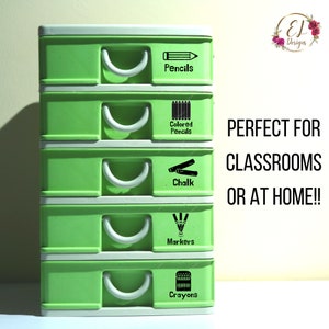 May include: A green plastic drawer organizer with five drawers. Each drawer has a white handle and a black label with a different art supply icon and text. The labels read: "Pencils", "Colored Pencils", "Chalk", "Markers", and "Crayons".