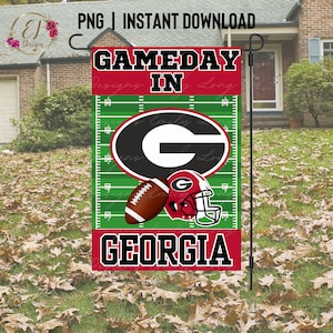 Puede incluir: Una bandera de jardín roja y verde con el texto "Gameday in Georgia" y un casco de fútbol y un balón de fútbol en un campo verde con líneas de yarda blancas. La letra "G" está en el centro de la bandera.