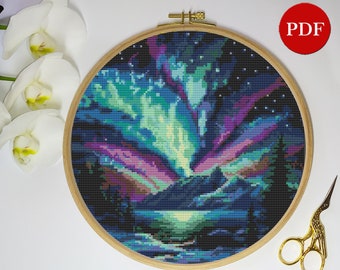 Puede incluir: Un patrón de punto de cruz que representa una aurora boreal colorida sobre una cordillera y un lago. El cielo es azul oscuro con estrellas blancas y la aurora es verde, morada y rosa.