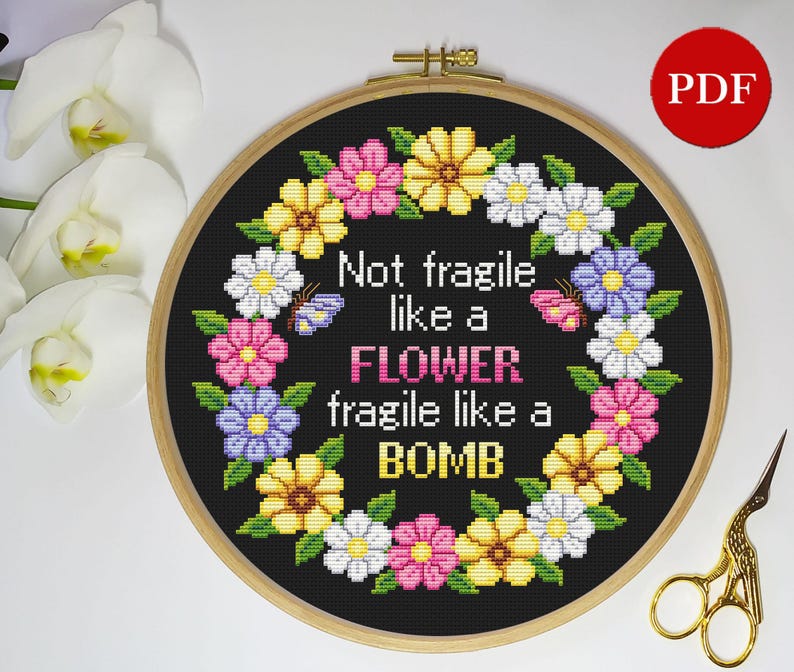 Puede incluir: Patr&oacute;n de punto de cruz con una corona de flores coloridas con el texto "Not fragile like a FLOWER fragile like a BOMB" sobre un fondo negro.