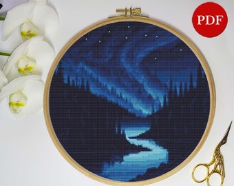 Puede incluir: Un patrón de punto de cruz de un cielo nocturno azul oscuro con un río serpenteando a través de un bosque. El cielo está lleno de estrellas blancas y una aurora boreal azul. El patrón está en un aro de bordado de madera.