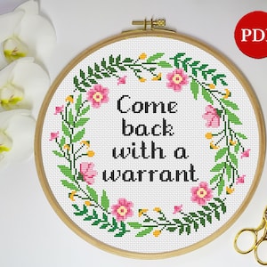 May include: A white embroidery hoop with a floral wreath design and the text "Come back with a warrant" in black lettering.