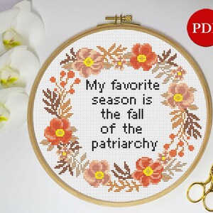 Puede incluir: Un aro de bordado de punto de cruz con fondo blanco y un dise&ntilde;o de corona floral. El texto en el centro dice "Mi estaci&oacute;n favorita es la ca&iacute;da del patriarcado".