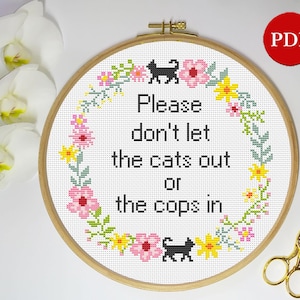 May include: A white embroidery hoop with a black cat and floral design. The text reads "Please don't let the cats out or the cops in."