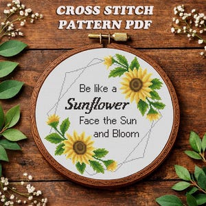 May include: A cross-stitch pattern in a wooden hoop featuring sunflowers and the text "Be like a Sunflower, Face the Sun and Bloom." The design includes yellow and green floral elements on a white background, with the words in black.