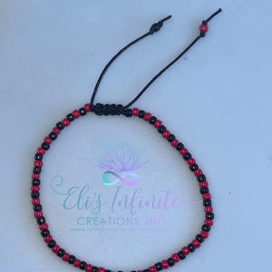 May include: Adjustable bracelet featuring alternating red and black beads. The bracelet is strung on a black cord with a sliding knot closure. The ends of the cord have small red beads. The bracelet is a simple, yet elegant accessory.
