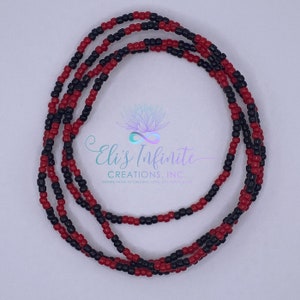 May include: A red and black beaded waist bead necklace. The beads are small and evenly spaced. The necklace is coiled and laid flat on a white surface.