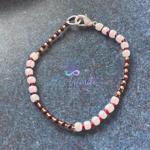 May include: A beaded bracelet featuring white, gold and burgundy beads. The bracelet has a silver clasp.