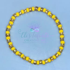 May include: A yellow and gold beaded bracelet. The bracelet is made of small, round beads that are strung together to form a circle.