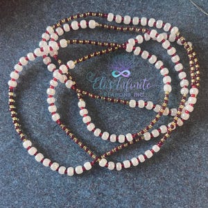 May include: A waist bead necklace with three strands of beads. The beads are white, burgundy and gold.