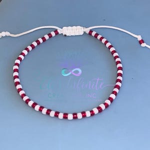 May include: A red and white beaded bracelet with a white string closure. The bracelet is made with small, round beads.