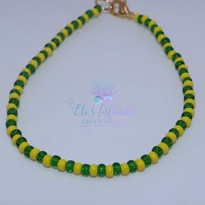 May include: A beaded bracelet featuring alternating yellow and green beads. The bracelet is secured with a gold-colored clasp. The text "Eli's Infinite Creations, Inc" is visible in the background.