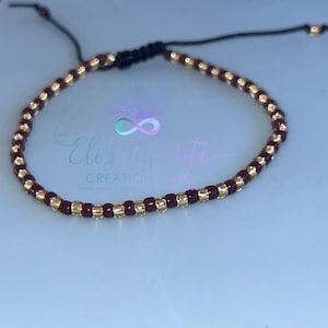 May include: A maroon and gold beaded bracelet with a black cord closure.