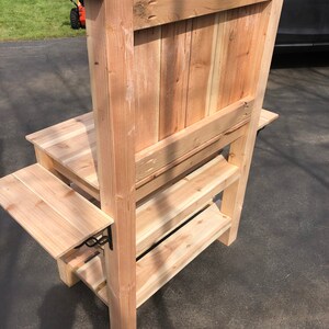 Puede incluir: Un banco de jard&iacute;n de madera con respaldo y dos estantes. El banco est&aacute; hecho de madera natural y tiene un aspecto r&uacute;stico.