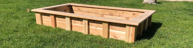 Puede incluir: Un lecho elevado de jard&iacute;n rectangular de madera de cedro. El lecho est&aacute; sobre un c&eacute;sped verde.