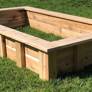 Puede incluir: Un lecho elevado de jard&iacute;n rectangular de madera de cedro. El lecho est&aacute; sobre un c&eacute;sped verde.