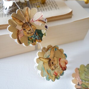 Peut inclure: Une guirlande de découpes de papier festonnées représentant des illustrations d'un lapin en vêtements vintage. La guirlande est enfilée sur une fine ficelle blanche. Les illustrations de lapins ont une esthétique vintage avec des couleurs douces.