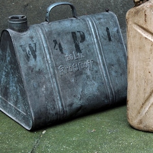 May include: Two vintage metal fuel cans. One is grey and has the text "W.P.I. 20 Ltr. Kraftstoff" on the side. The other is beige and has the text "Kraftstoff 20 Liter.  Reichsmark" on the side.