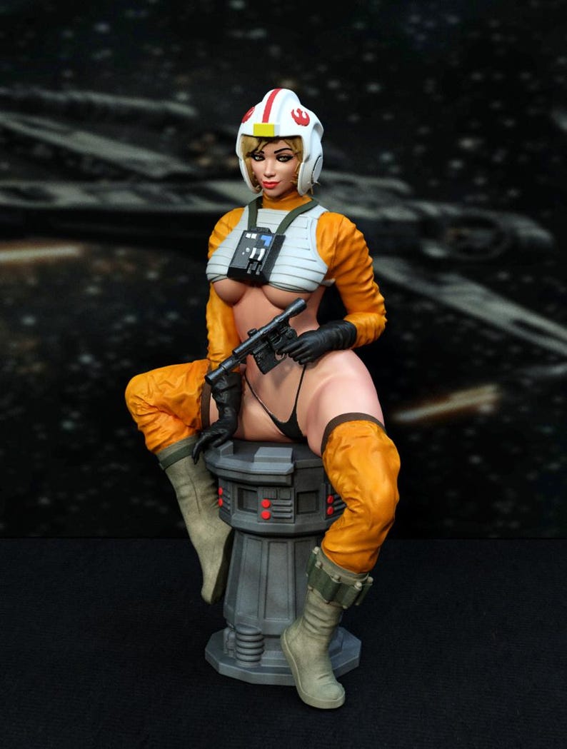 May include: A female action figure wearing an orange and white flight suit with a helmet and holding a blaster. The figure is sitting on a gray platform with red lights.