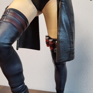 May include: A black leather figure with a black and red belt and a black leather skirt. The figure is wearing black leather boots and has a black leather strap on the left leg.