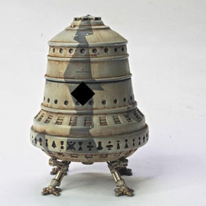 May include: A model of a gray and brown spaceship with a black diamond on the side. The spaceship has three legs and a rounded top.