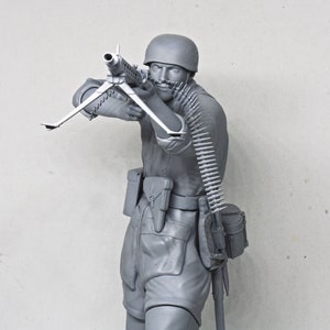 May include: A gray plastic model of a soldier holding a machine gun. The soldier is wearing a helmet and has a belt of ammunition around his waist.
