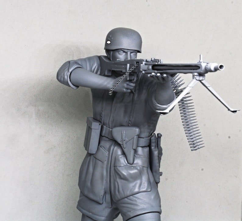 May include: A gray plastic model of a soldier holding a machine gun with a long ammunition belt. The soldier is wearing a helmet and a uniform with a belt and pouches.