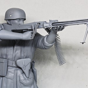 May include: A gray plastic model of a soldier holding a machine gun with a bipod. The soldier is wearing a helmet and a belt with a pouch. The machine gun has a long barrel and a belt of ammunition.