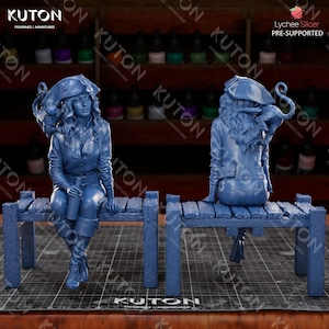 Pode incluir: Uma figura em miniatura de pirata feminina impressa em 3D de cor azul, sentada em um banco de madeira. A pirata est&aacute; vestindo uma jaqueta azul, cal&ccedil;as azuis e um chap&eacute;u de pirata. Ela est&aacute; segurando uma garrafa na m&atilde;o. A figura est&aacute; em pose com as pernas cruzadas e os bra&ccedil;os apoiados no banco. A figura &eacute; impressa em azul claro e tem um acabamento liso.