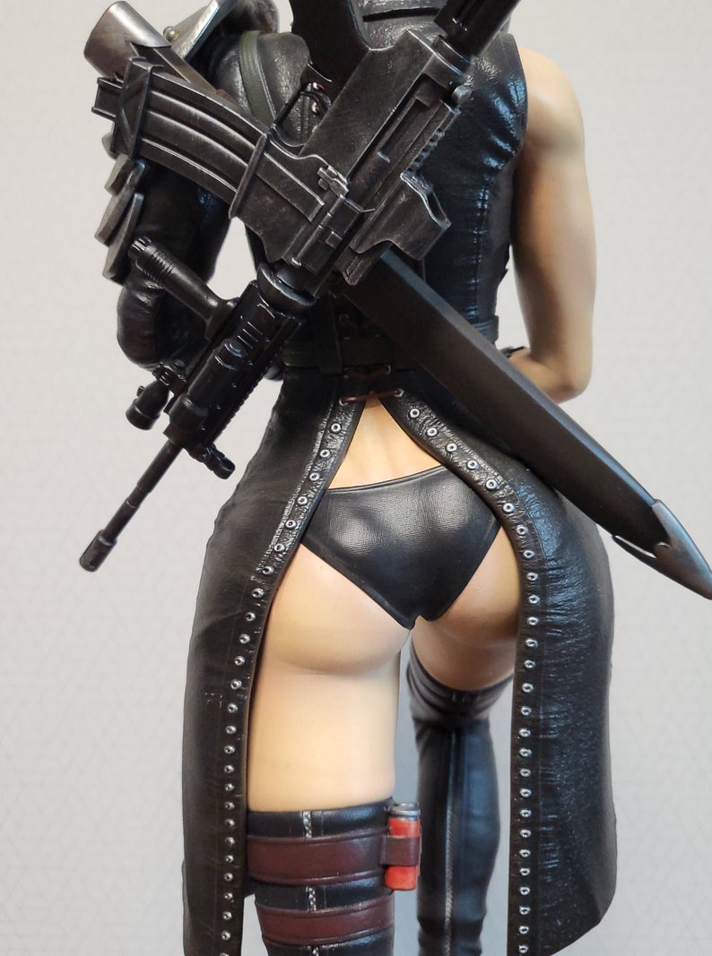 May include: A black leather outfit with a long skirt and a high-cut leg opening. The outfit features a black leather belt and a black leather bra. The figure is holding a black rifle and a black sword.