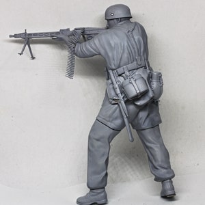 May include: A gray plastic model of a soldier holding a machine gun. The soldier is wearing a helmet and a uniform with a belt and pouches. The machine gun has a long barrel and a bipod.