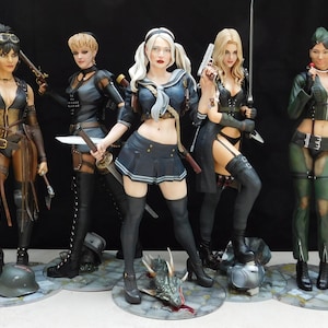 K&ouml;nnte beinhalten: F&uuml;nf weibliche Actionfiguren in verschiedenen Posen, jede mit einer Waffe. Die Figuren sind in verschiedenen Outfits gekleidet, darunter eine schwarze Lederjacke, eine Matrosenuniform und eine gr&uuml;ne Milit&auml;rjacke. Die Figuren stehen auf runden Sockeln mit verschiedenen Details, darunter ein Sch&auml;del, ein Drache und ein Helm.