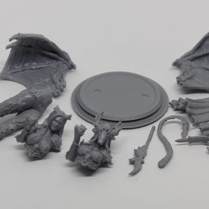 May include: A gray, unassembled fantasy miniature figure, featuring a female demon with wings, a tail, and various weapons. Includes a base and multiple parts for assembly. Ideal for tabletop gaming or collecting.