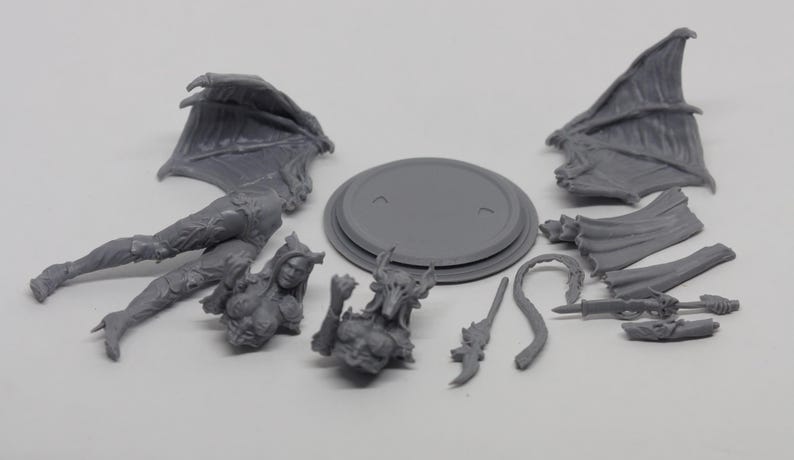 May include: A gray, unassembled fantasy miniature figure, featuring a female demon with wings, a tail, and various weapons. Includes a base and multiple parts for assembly. Ideal for tabletop gaming or collecting.