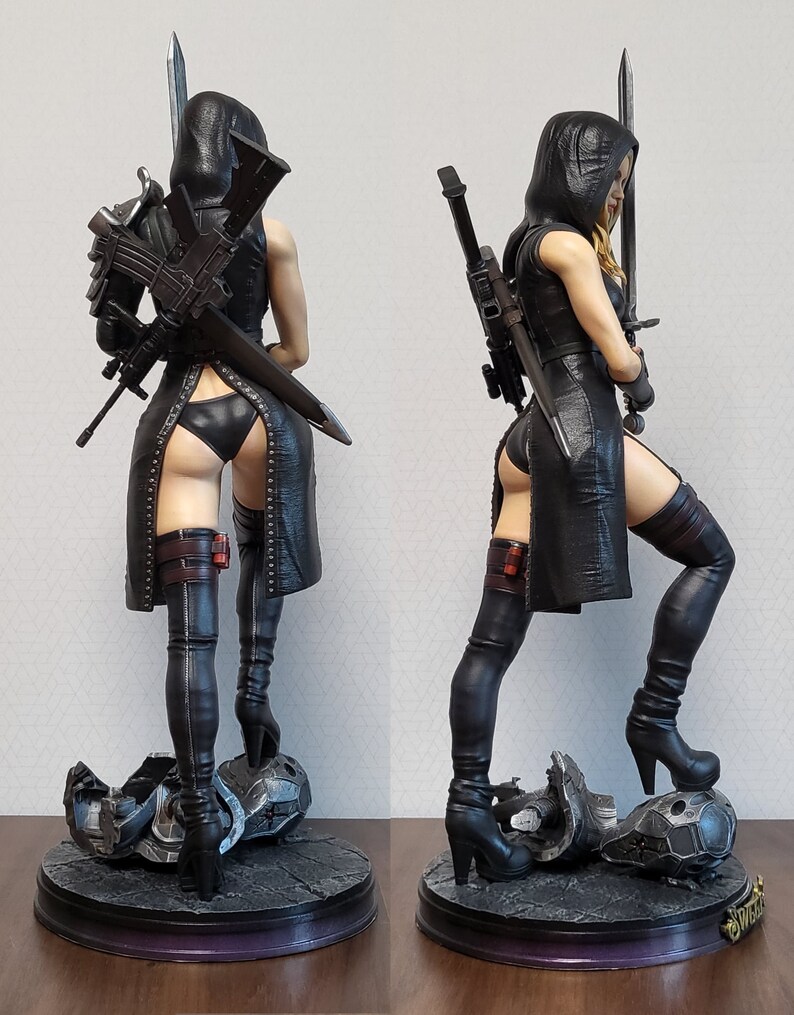 May include: A black and silver action figure of a female character wearing a black leather outfit, thigh-high boots, and a hooded cloak. She is holding a sword in one hand and a gun in the other. The figure is standing on a base with a broken piece of machinery.